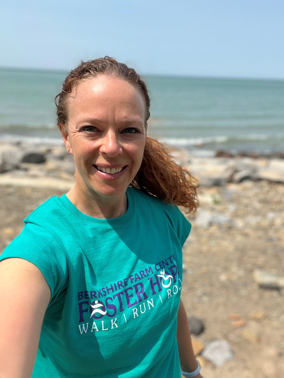 A woman with curly hair smiling at the camera in front of a seaside backdrop, wearing a teal