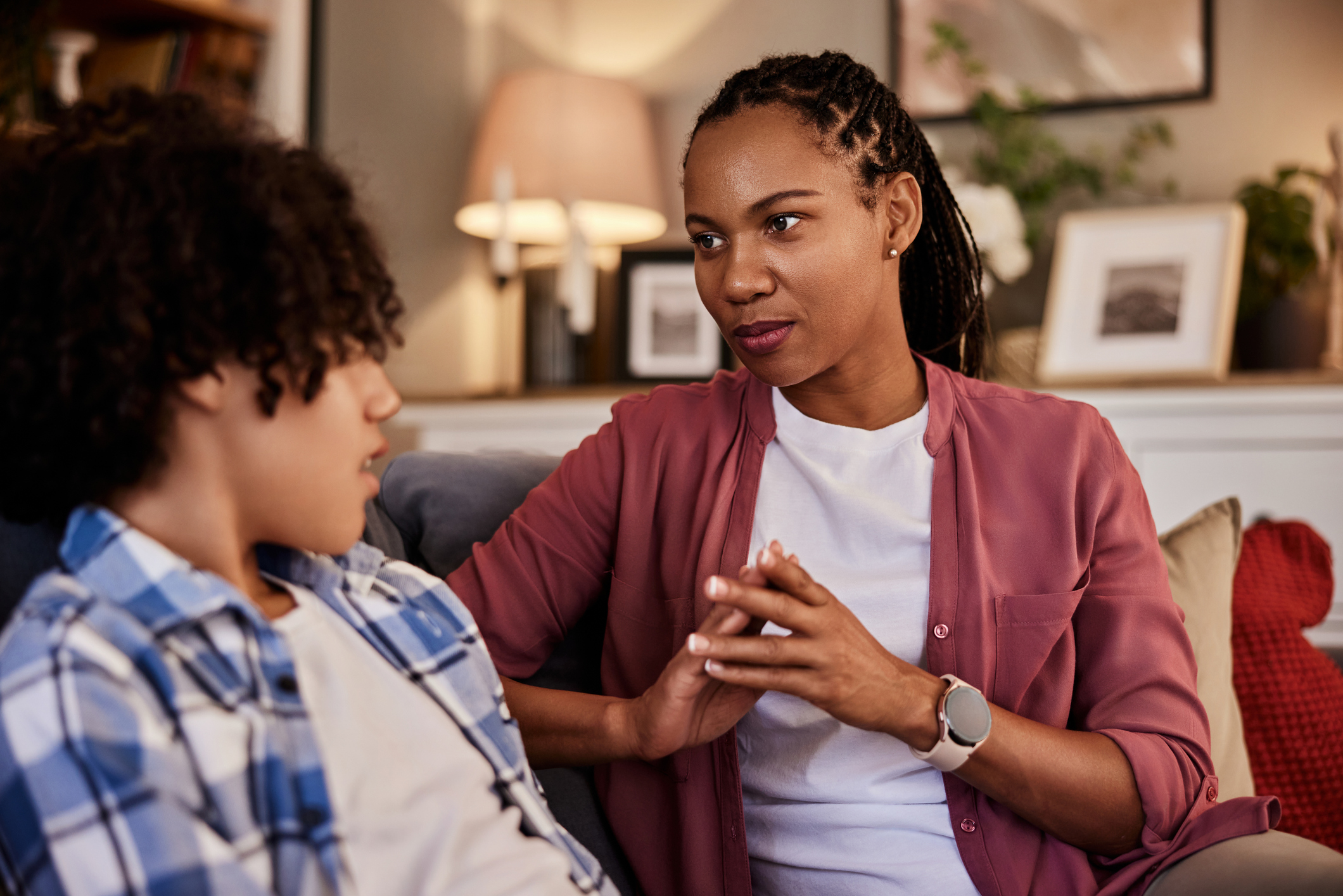 An African-American mother and her teenage son talking while sitting on a couch at home.