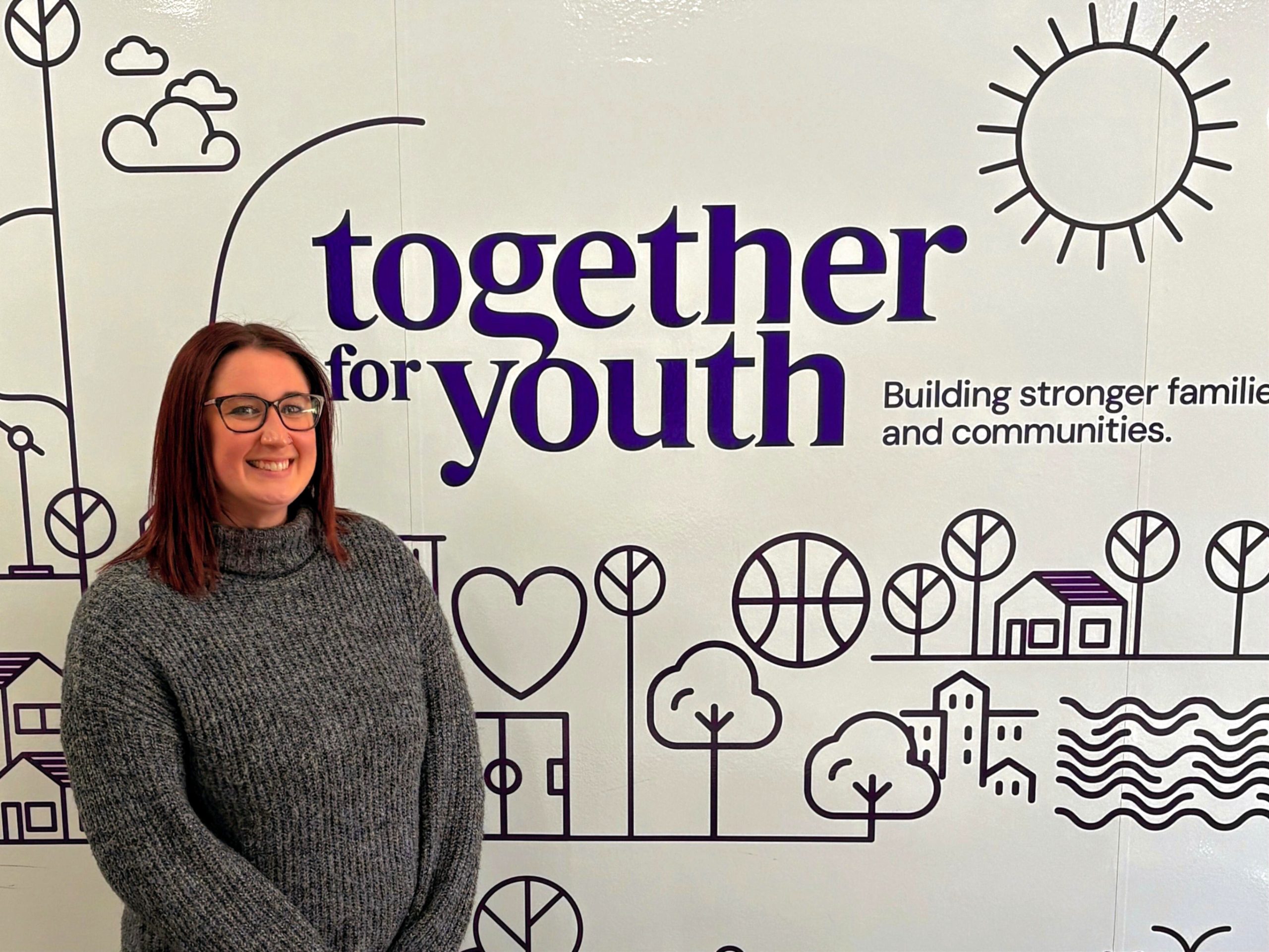 A woman stands to the left, smiling and looking at the camera. On the wall behind her is purple icons including hearts, trees, and sun. The words Together for Youth are displayed as part of the design.